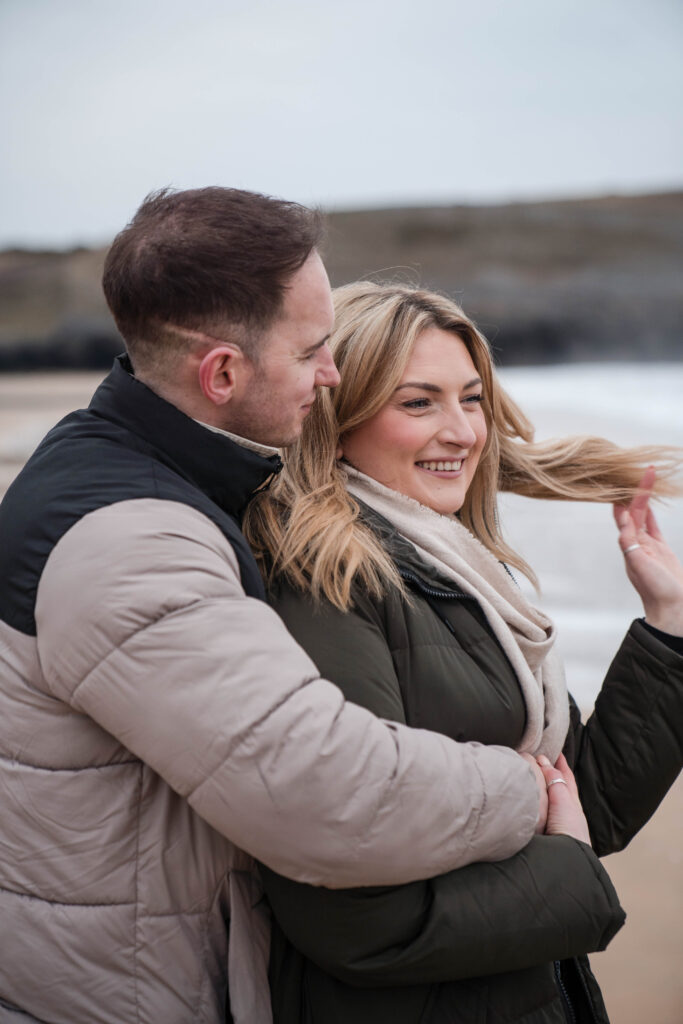 Engagement photoshoot of couple on the beach at Broad Haven South, Pembrokeshire, West Wales. Couple laughing and hugging