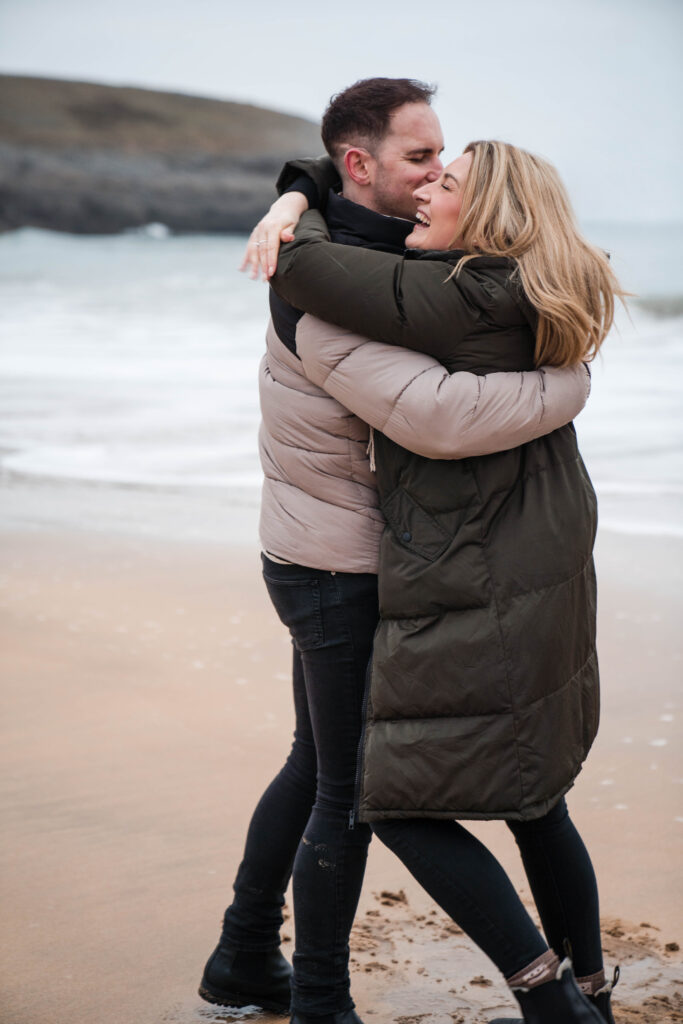 Engagement photoshoot of couple on the beach at Broad Haven South, Pembrokeshire, West Wales. Couple laughing and hugging